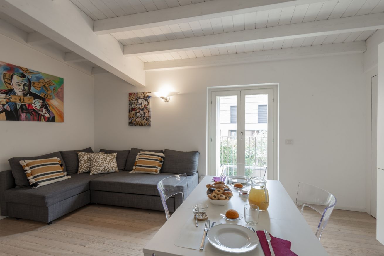 A modern living room with a grey sofa, a dining table with a white tablecloth, and artwork on the walls.
