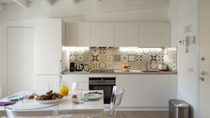 Una cocina moderna con armarios blancos, un salpicadero con diseño y un comedor con sillas transparentes y una mesa dispuesta para dos.