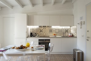 A modern kitchen with white cabinetry, a patterned backsplash, and a dining area with clear chairs and a table set for two. - UMBRIA, 120 - Cozy and well-connected (Milano)