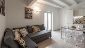 Una sala de estar moderna con un sofá gris, sillas transparentes, una mesa de comedor y una zona de cocina.
