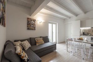 A modern living room with a grey sofa, clear chairs, a dining table, and a kitchen area. - UMBRIA, 120 - Cozy and well-connected (Milano)