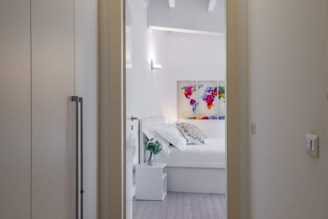 A modern bedroom with a bed, a nightstand, a wall art piece, and a white wardrobe.