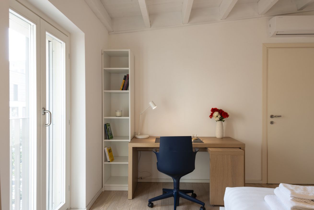 A bedroom with a bed, a desk, a chair, a bookshelf, and a door.