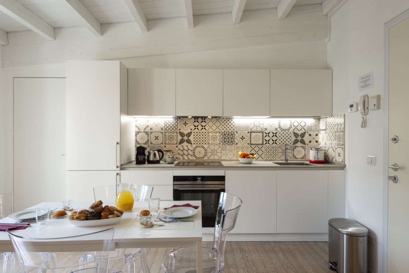 Eine moderne Küche mit weißen Schränken, einer gemusterten Spritzschutzwand und einem Essbereich mit transparenten Stühlen und einem Tisch für zwei Personen.