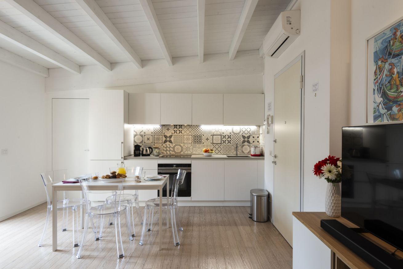 A modern kitchen with white cabinets, a patterned backsplash, and a dining area with clear chairs.