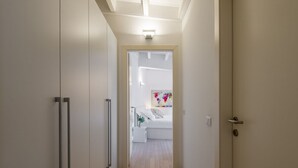Un pasillo que conduce a un dormitorio con una cama, una mesita de noche y una lámpara fijada a la pared.