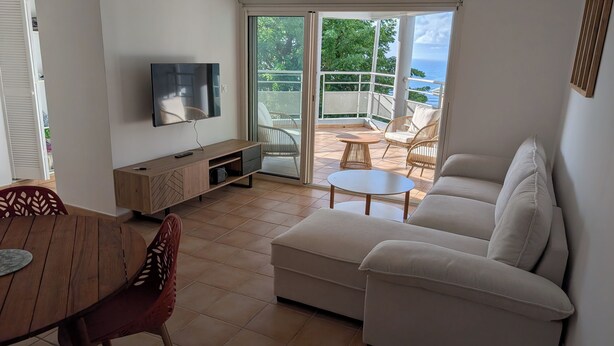 A living room with a TV, sofa, and dining area. - Ocean view appartement up to one of the most beautiful beach of the island (Le Gosier)