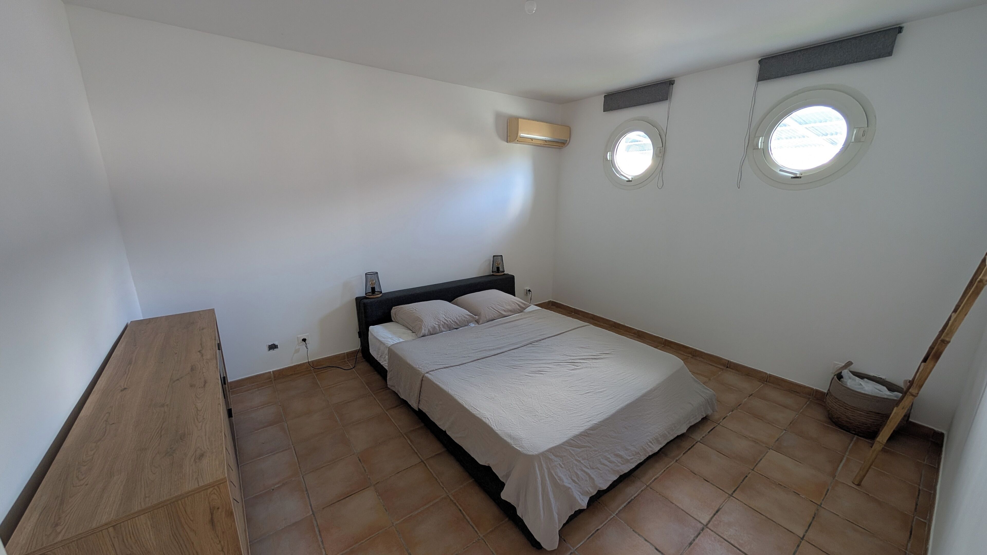 Une chambre à coucher comprenant un lit, une table de chevet, un banc en bois, une fenêtre et un ventilateur de plafond.