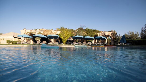 A clear swimming pool with lounge chairs and umbrellas, surrounded by a building with a traditional architectural style. - Bungalow Nature & Bien-Être near Marrakech | Swimming pool, Hammam & Tranquility (Marrakech)