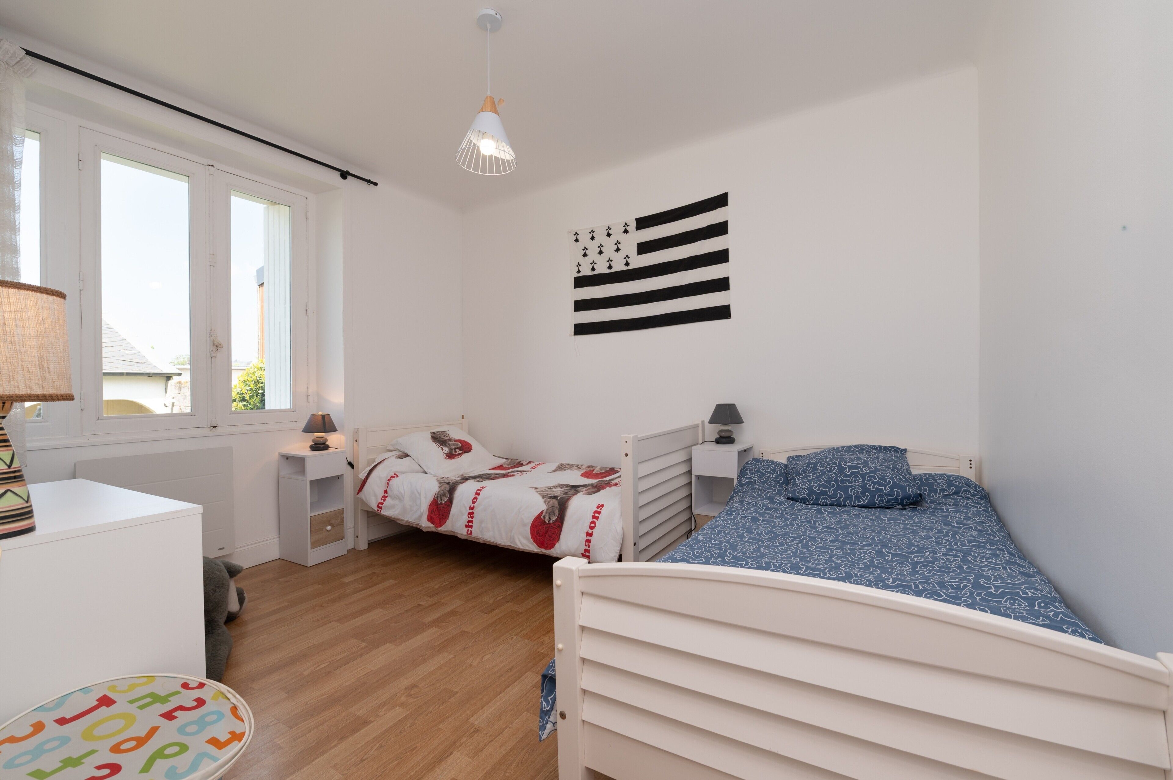Une chambre avec deux lits, une fenêtre, une lampe et un élément décoratif mural.