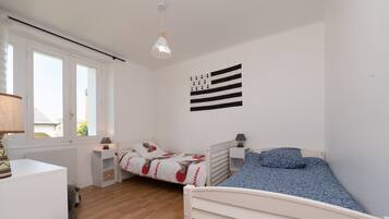 Une chambre avec deux lits, une fenêtre, une lampe et un élément décoratif mural.