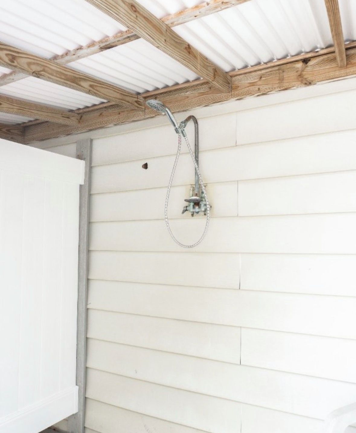 A shower with a metal hose and a white wall with horizontal siding.