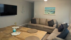 A living room with a sofa, a coffee table, a TV mounted on the wall, and a framed picture. - Peaceful 2-bedroom condo in Wildwood Crest, close to beach (Wildwood)