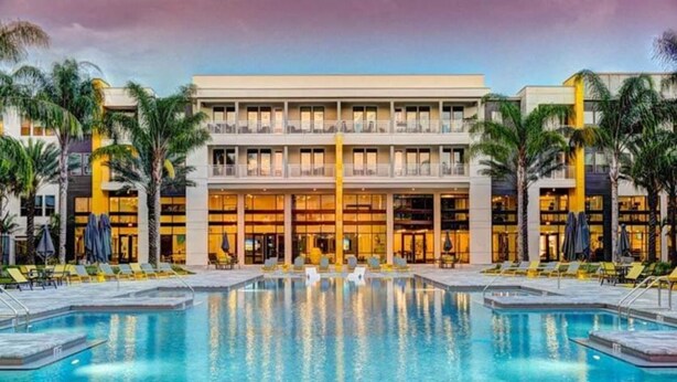 A hotel with a large outdoor swimming pool, multiple balconies, and palm trees. - Spacious 1-BR, 2-King Beds, Near Mayo, Pool, Gym, Fast Wifi Workspace, Beach (Jacksonville)