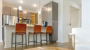 A modern kitchen with stainless steel appliances, wooden cabinets, and three bar stools with woven seats. - Spacious 1-BR, 2-King Beds, Near Mayo, Pool, Gym, Fast Wifi Workspace, Beach (Jacksonville)