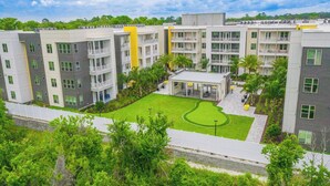 A multi-story residential building with balconies, a central courtyard with a lawn, and surrounding greenery. - Spacious 1-BR, 2-King Beds, Near Mayo, Pool, Gym, Fast Wifi Workspace, Beach (Jacksonville)