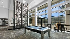 A pool table in a spacious room with large windows, a sofa, and a dining area. - Spacious 1-BR, 2-King Beds, Near Mayo, Pool, Gym, Fast Wifi Workspace, Beach (Jacksonville)