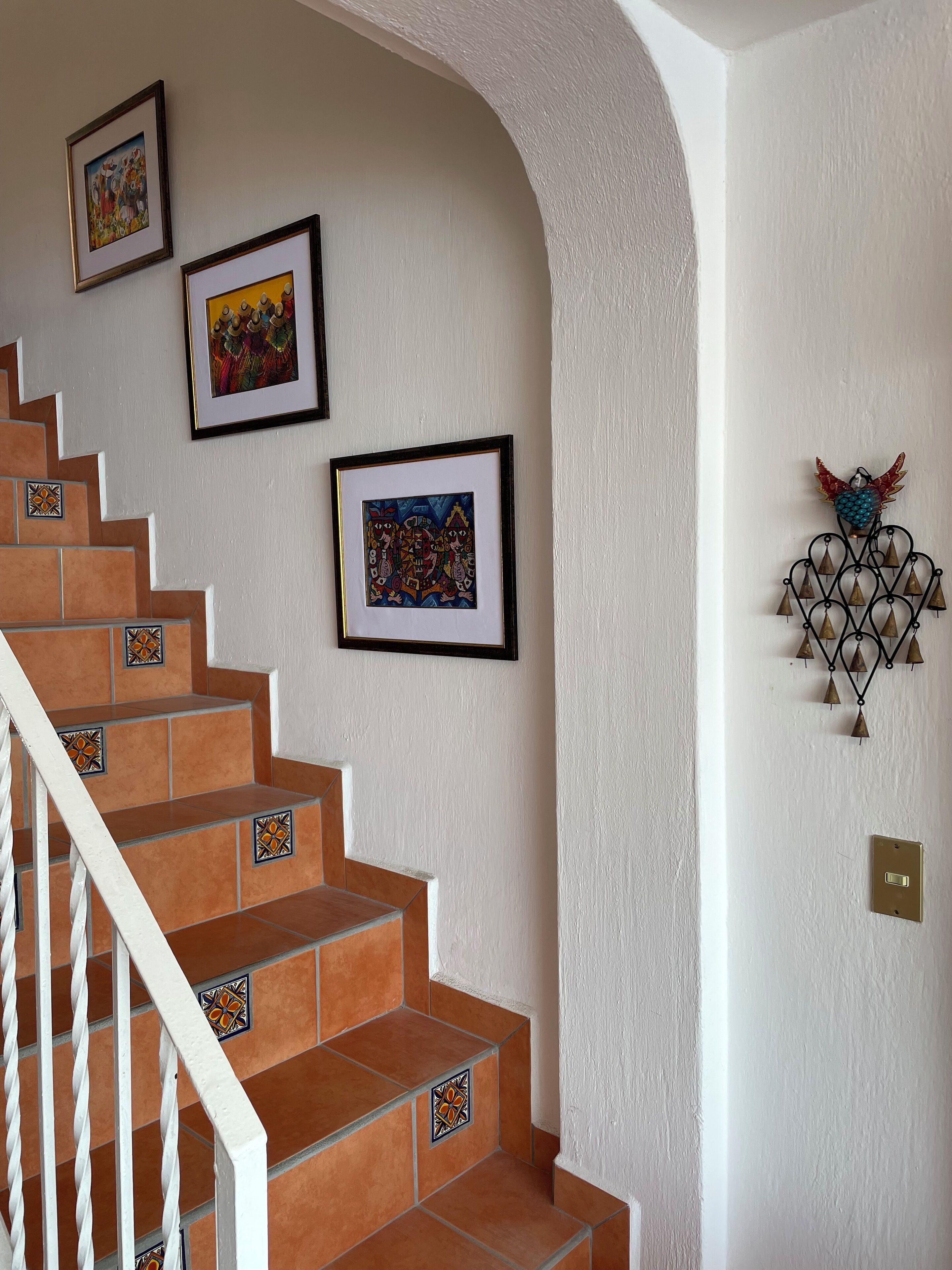 A staircase with orange tiles and decorative tiles at the base, leading to a landing with framed artwork and a wall-mounted decorative piece.