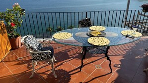Et glasbord med udsigt over havet, en stol og en potteplante på en terrasse.