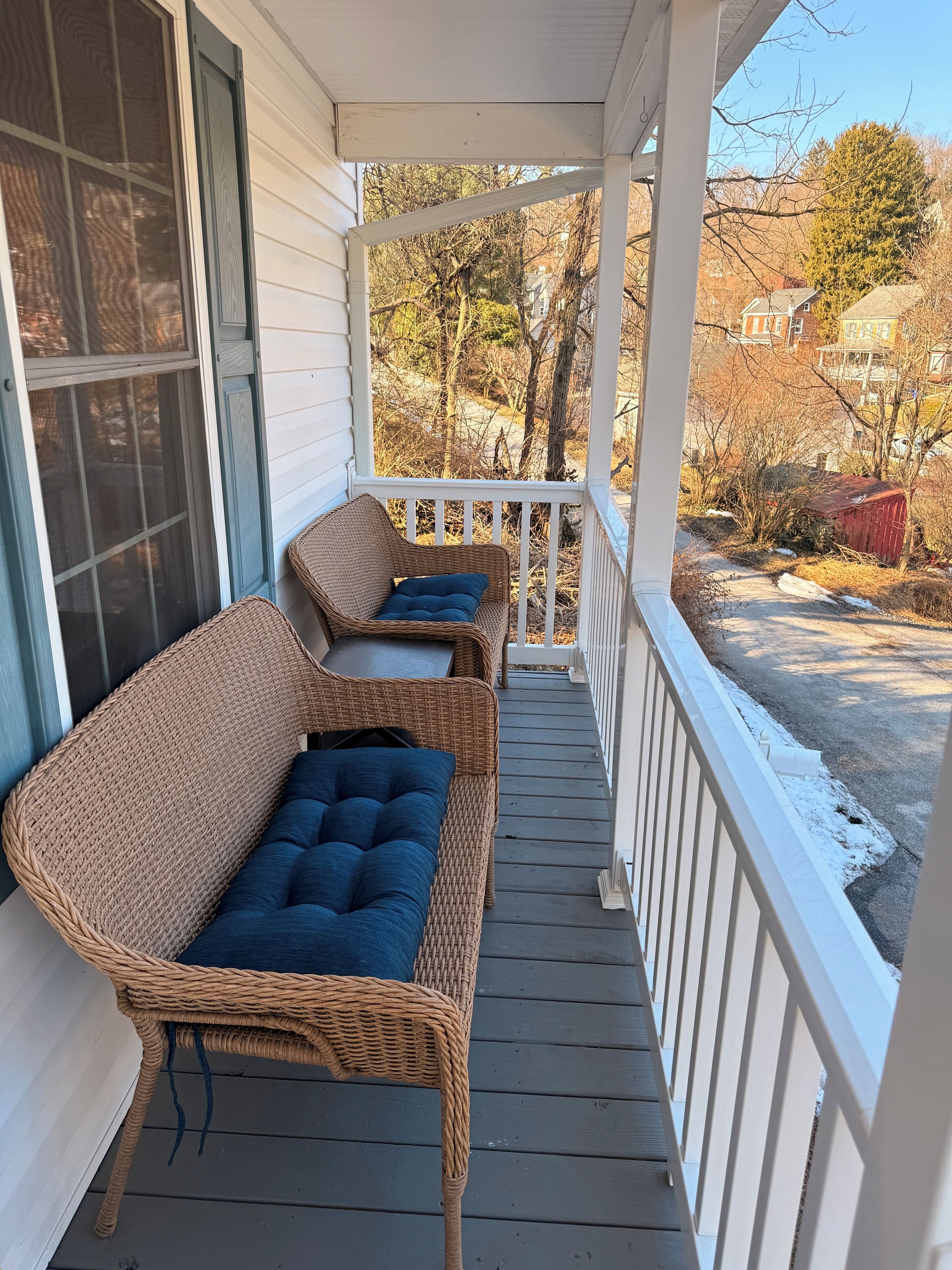 A covered porch with wicker furniture and a view of a residential area.