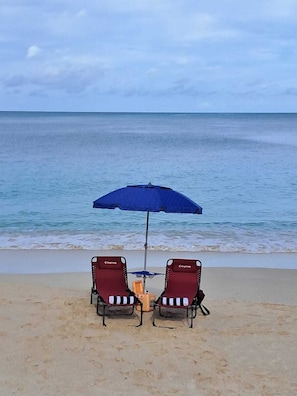 Una spiaggia con due lettini rossi e un ombrellone blu.