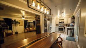 A modern kitchen with white cabinets, a stainless steel refrigerator, and a microwave. There is a dining area with a wooden table and chairs. - Soak Under the Stars - Hot Tub, AC, Downtown Bungalow (Flagstaff)