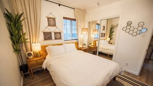 A neatly arranged bedroom with a large bed, bedside lamps, a mirror, and a wall-mounted hexagonal decoration. - Soak Under the Stars - Hot Tub, AC, Downtown Bungalow (Flagstaff)