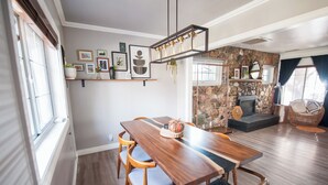 A dining area with a wooden table and chairs, a stone wall, and a fireplace. - Soak Under the Stars - Hot Tub, AC, Downtown Bungalow (Flagstaff)