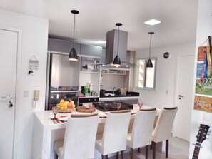 A modern kitchen with white cabinetry, a central island with a stove, and pendant lighting. - S FLATS MOTA BEIRA MAR (Fortaleza)