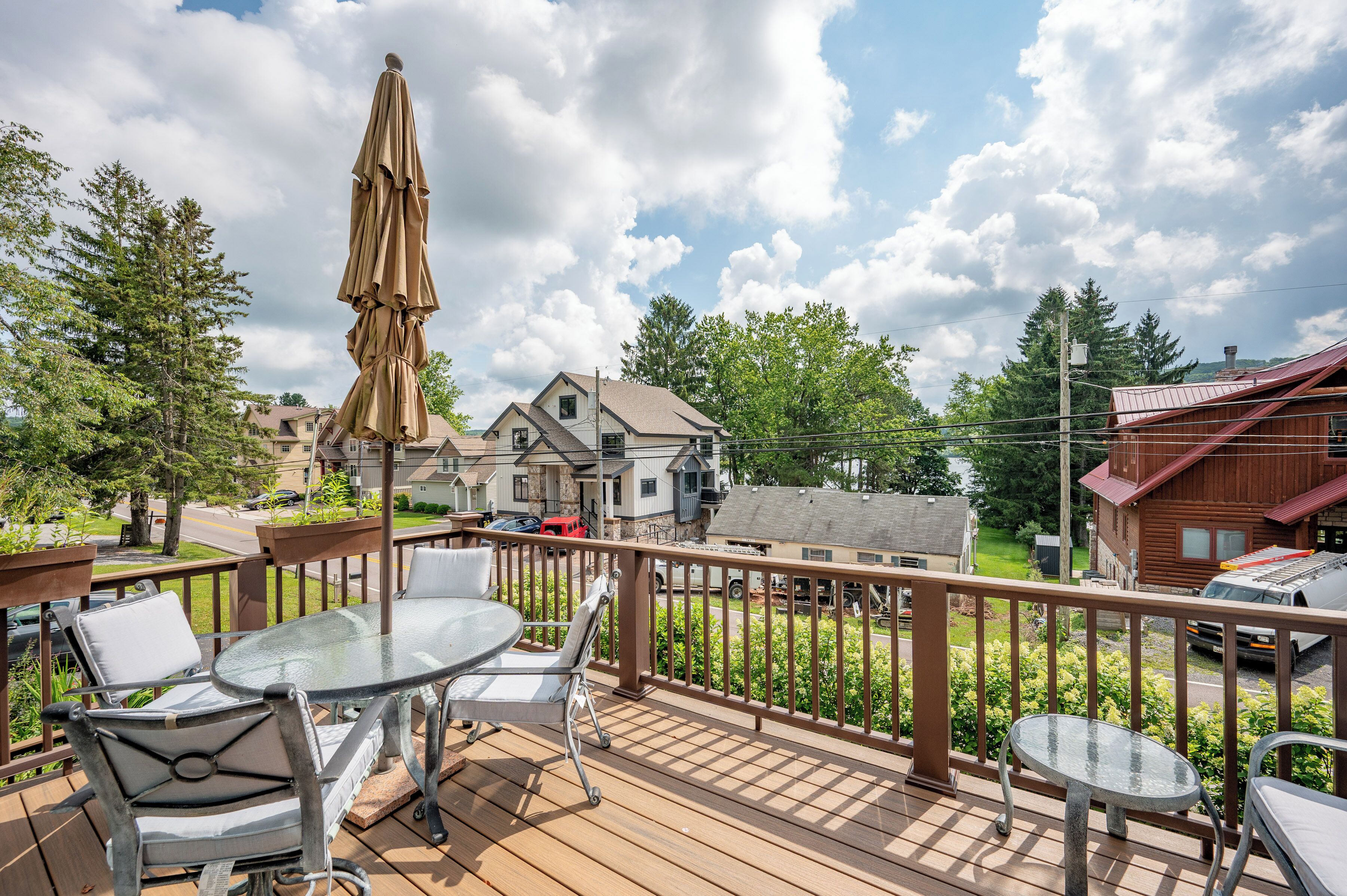 A wooden deck with a glass table and chairs, an umbrella, and a view of houses and trees.