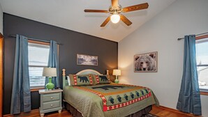 A bedroom with a bed, nightstands, a ceiling fan, and two windows with curtains.