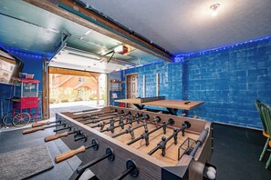 A foosball table in a room with a blue brick wall, a wooden table, and a bicycle in the background.