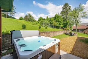 Ein Whirlpool in einem Hinterhof mit einer Holzterrasse, einer überdachten Sitzgelegenheit und Blick auf einen Hügel mit Bäumen.