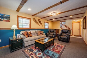 A living room with a sofa, two armchairs, a coffee table, a rug, and a staircase. - New! Modern Lakeview Ski Retreat w/ Hot Tub (McHenry)