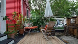 A patio with outdoor furniture, a white umbrella, and a red building in the background. - Charming Historic Bungalow w/ Loft & Private Basement Suite (Houston)