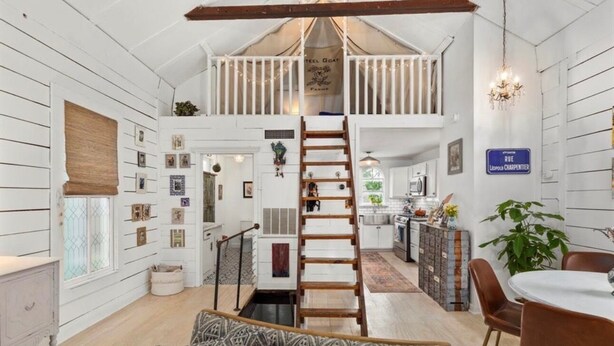 A loft-style room with a wooden ladder leading to a lofted area, a dining table with chairs, and a kitchen in the background. - Charming Historic Bungalow w/ Loft & Private Basement Suite (Houston)