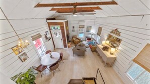 A spacious room with a high ceiling, wooden beams, a dining area with a table and chairs, a sofa, and a small kitchen area. - Charming Historic Bungalow w/ Loft & Private Basement Suite (Houston)