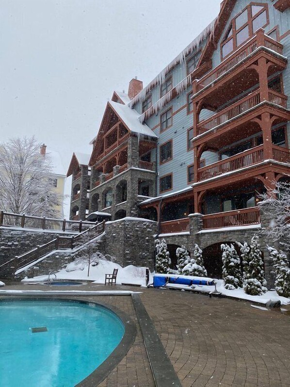 Un immeuble à plusieurs étages, doté d’une façade en pierre, de balcons en bois et d’un espace piscine avec une terrasse en briques.