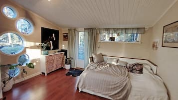 A bedroom with a large bed, a dresser, a television, and multiple windows.