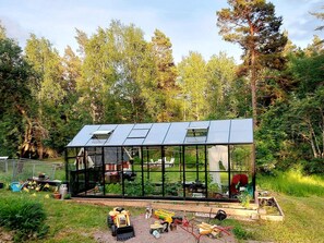 Una casa moderna de vidrio con techo inclinado, rodeada de jardín y árboles.