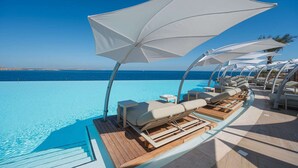Ein Pool ohne Ende mit weißen Sonnenschirmen und Liegestühlen mit Blick auf das Meer.