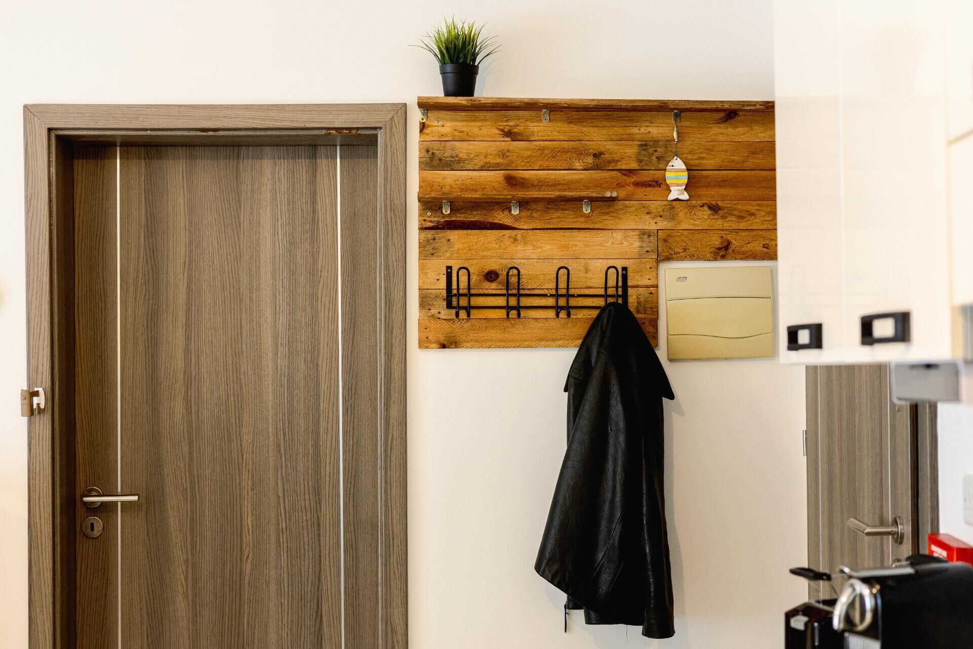 A wooden door, a coat rack with a jacket, a small plant, and a wall-mounted heater.