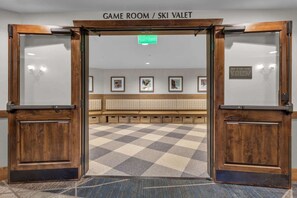 A hotel entrance with a checkered floor, a sign above the doors reading "GAME ROOM / SKI VALET", and framed pictures on the wall. - Sunrise Gondola Getaway - Ski In/ski Out (Park City)
