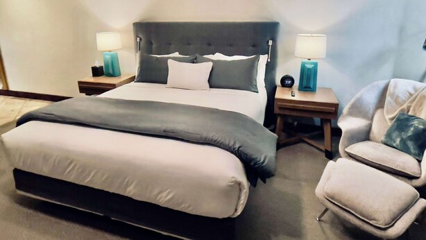 A hotel room with a large bed, two bedside tables with lamps, a chair, and a nightstand with a clock. - Sunrise Gondola Getaway - Ski In/ski Out (Park City)