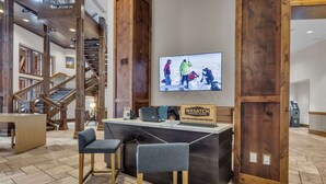 A reception area with a wooden staircase, a reception desk, and a television displaying an outdoor scene. - Sunrise Gondola Getaway - Ski In/ski Out (Park City)