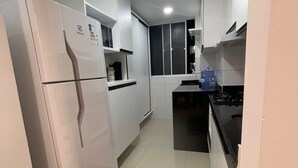 A compact kitchen with white cabinets, a built-in refrigerator, a stove, and a microwave. - Bright 2-bedroom apartment with AC in beautiful Natal -Cotovelo (Parnamirim)