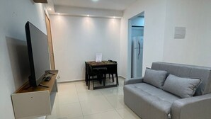 A modern living room with a flat-screen TV, a grey sofa, and a dining table with chairs. - Bright 2-bedroom apartment with AC in beautiful Natal -Cotovelo (Parnamirim)