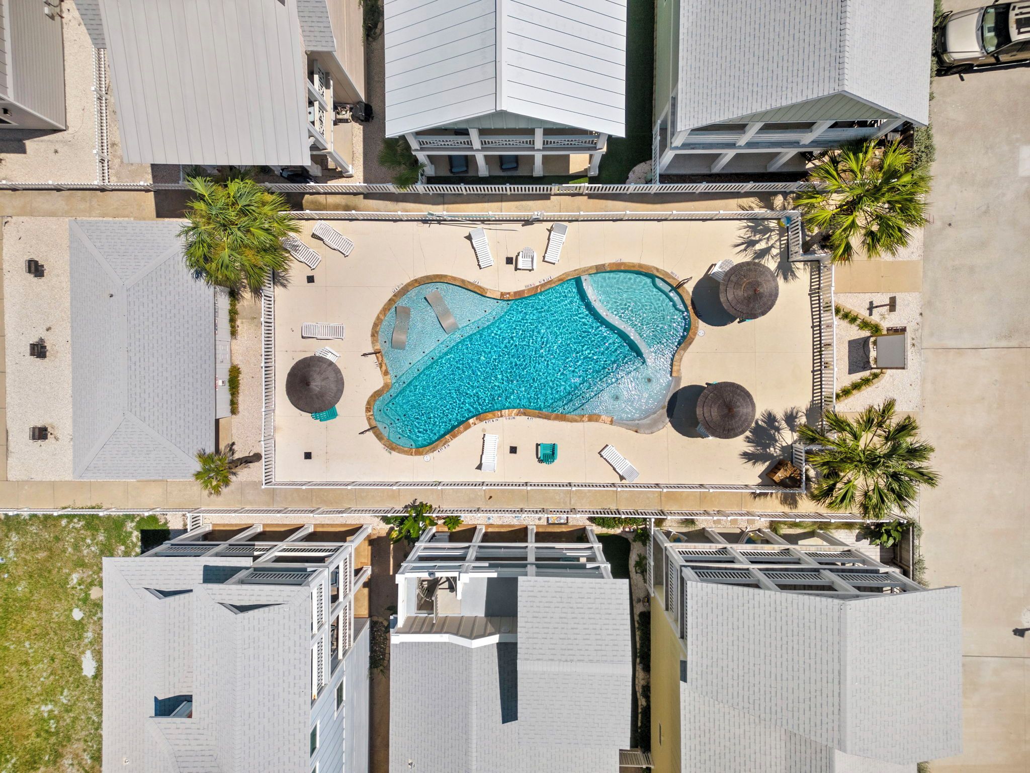 An aerial view of a resort with a central swimming pool, multiple buildings, and palm trees.
