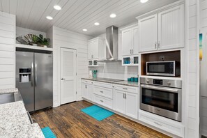 A modern kitchen with white cabinetry, stainless steel appliances, and a wooden floor. - Dauphin Beach House (Port Aransas)