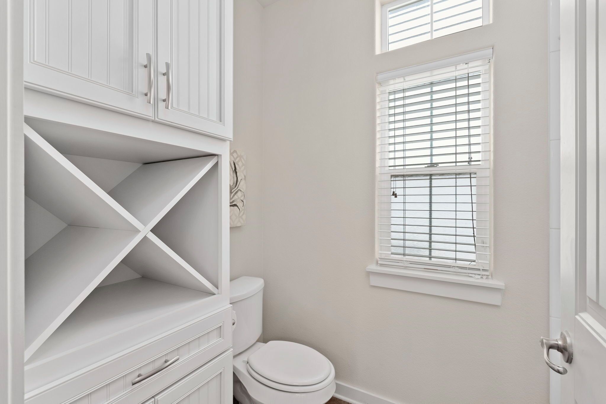 A bathroom with a toilet, a white cabinet, and a window with blinds.